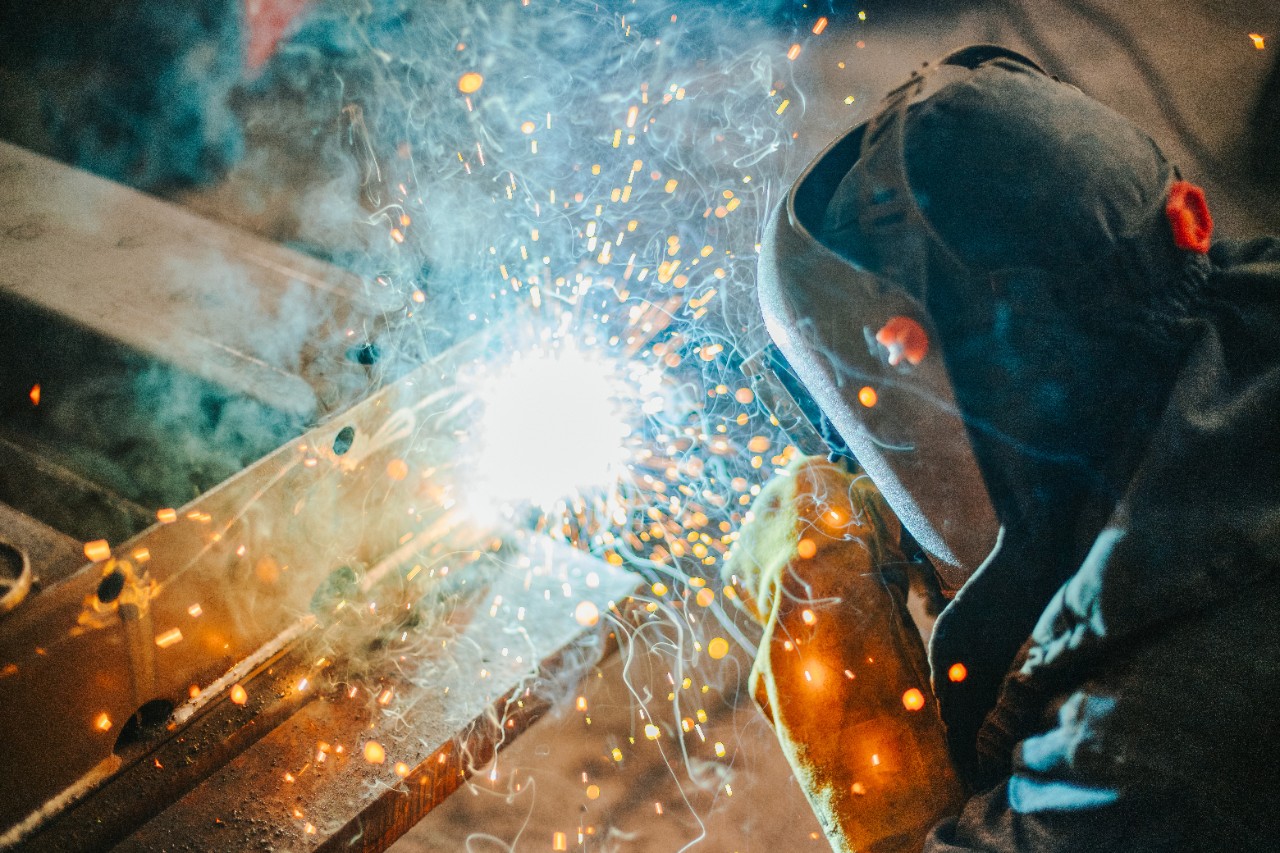 Um soldador usando equipamento de proteção enquanto une duas peças de metal.