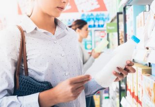 Stock Photography: Woman shopping at the supermarket, she is holding a milk bottle and reading her shopping list